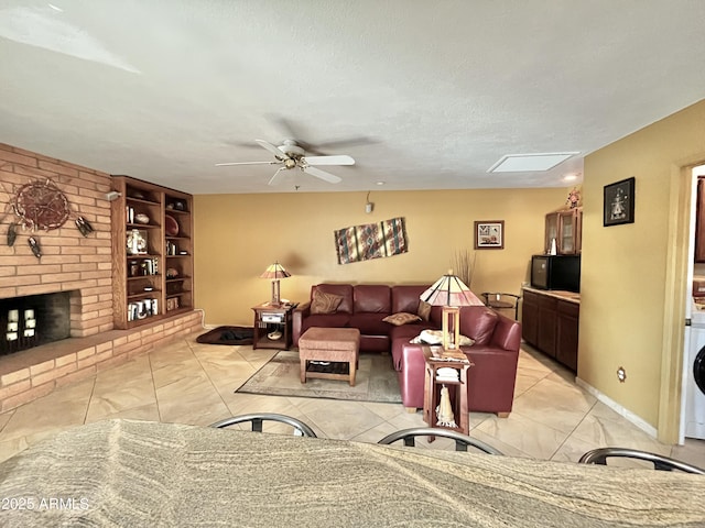 living room featuring a skylight, ceiling fan, a brick fireplace, built in features, and a textured ceiling