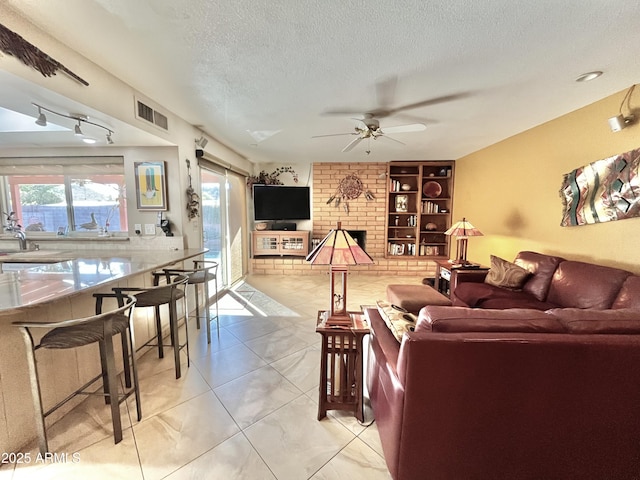 living room featuring ceiling fan, a textured ceiling, and a brick fireplace