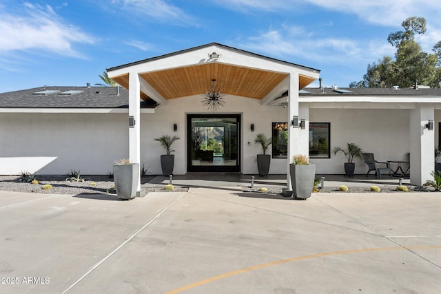 view of exterior entry featuring roof with shingles and stucco siding