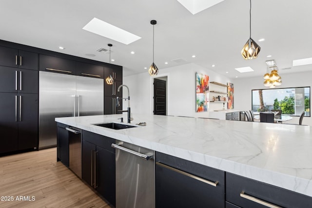 kitchen featuring visible vents, a skylight, dark cabinetry, a sink, and decorative light fixtures