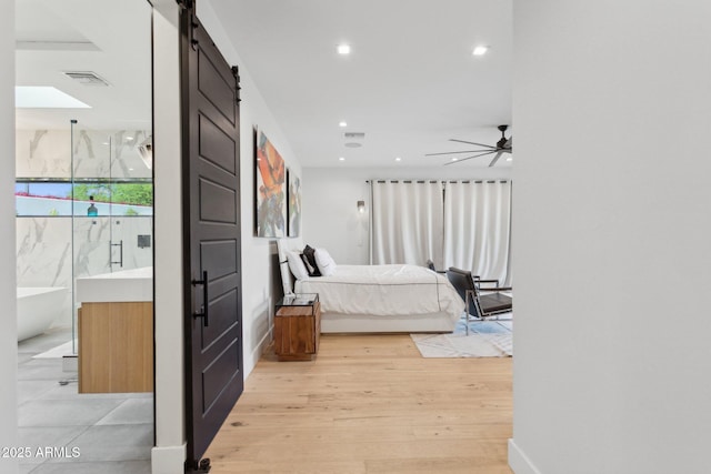 bedroom with a barn door, light wood-style floors, recessed lighting, baseboards, and visible vents