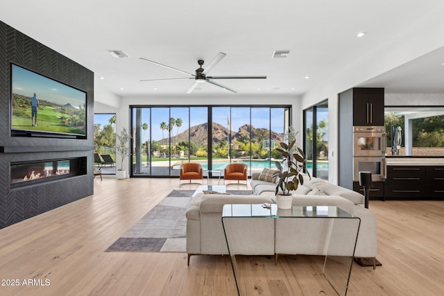 living room featuring a fireplace, a ceiling fan, light wood-style flooring, and visible vents