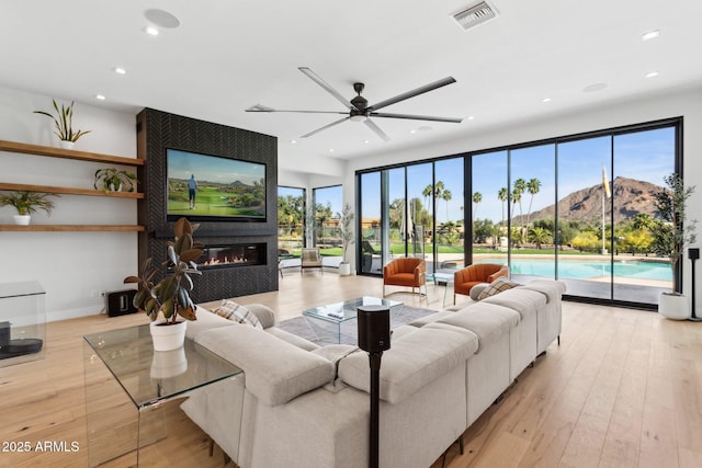 living area with light wood-style floors, ceiling fan, visible vents, a glass covered fireplace, and recessed lighting