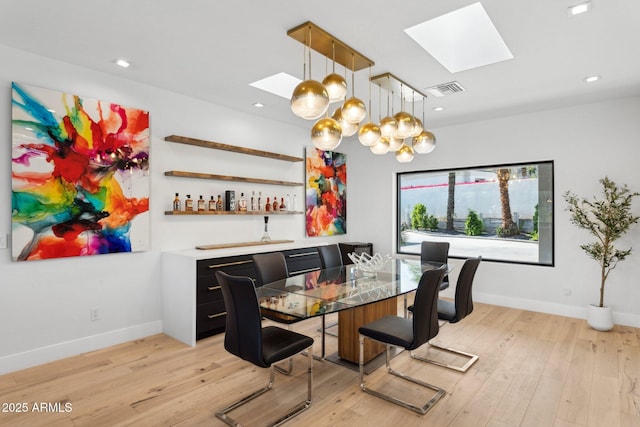dining area featuring baseboards, light wood finished floors, visible vents, and a skylight