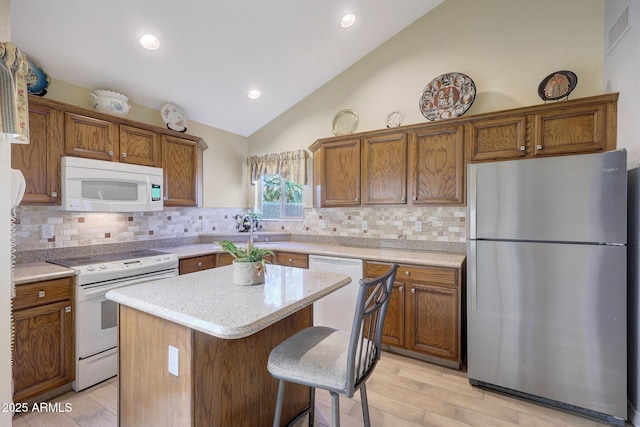 kitchen with vaulted ceiling, a kitchen island, decorative backsplash, sink, and white appliances