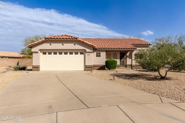 mediterranean / spanish home with a tile roof, stucco siding, concrete driveway, an attached garage, and fence