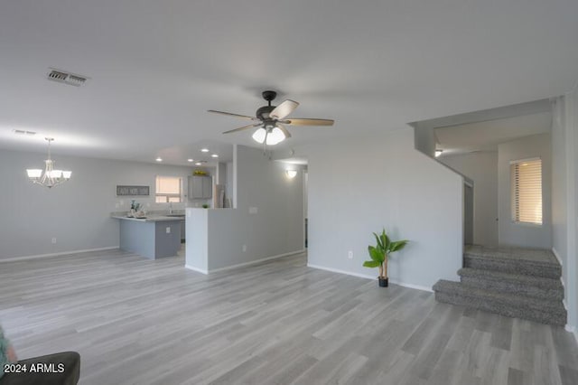 unfurnished living room featuring ceiling fan with notable chandelier and light hardwood / wood-style floors