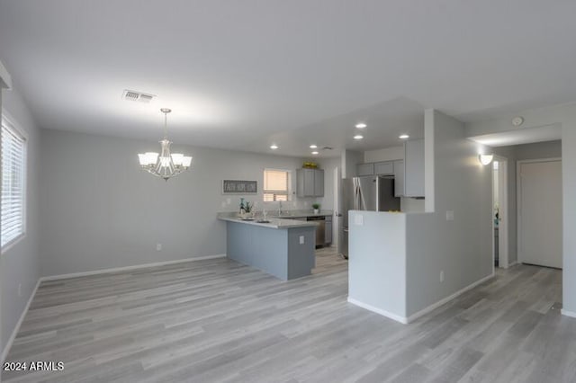 kitchen featuring kitchen peninsula, gray cabinetry, stainless steel appliances, an inviting chandelier, and light hardwood / wood-style flooring