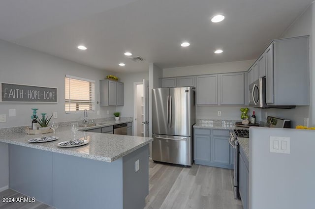 kitchen with kitchen peninsula, appliances with stainless steel finishes, light hardwood / wood-style floors, and sink