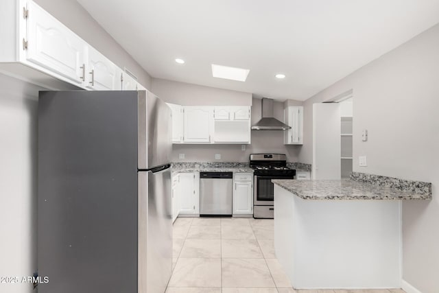 kitchen featuring a peninsula, a skylight, white cabinets, wall chimney range hood, and appliances with stainless steel finishes