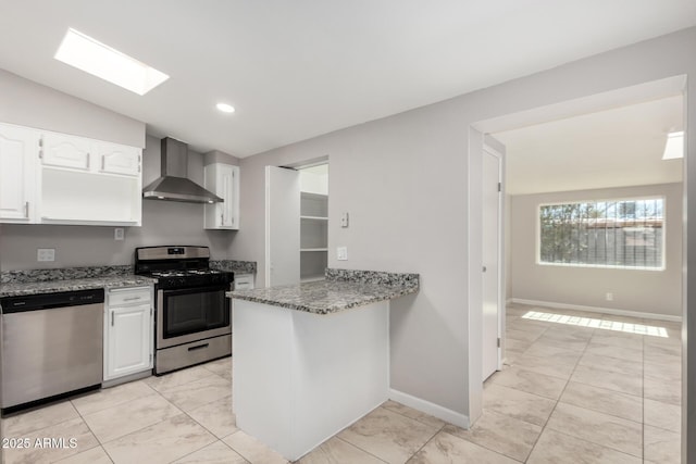 kitchen featuring stainless steel appliances, white cabinetry, wall chimney range hood, light stone countertops, and vaulted ceiling with skylight