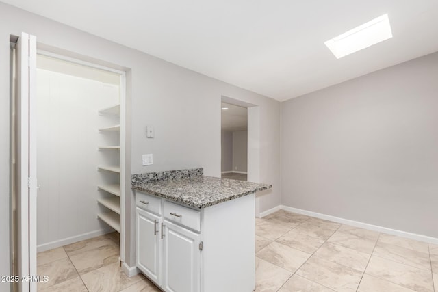 kitchen with light stone counters, a peninsula, a skylight, baseboards, and white cabinets