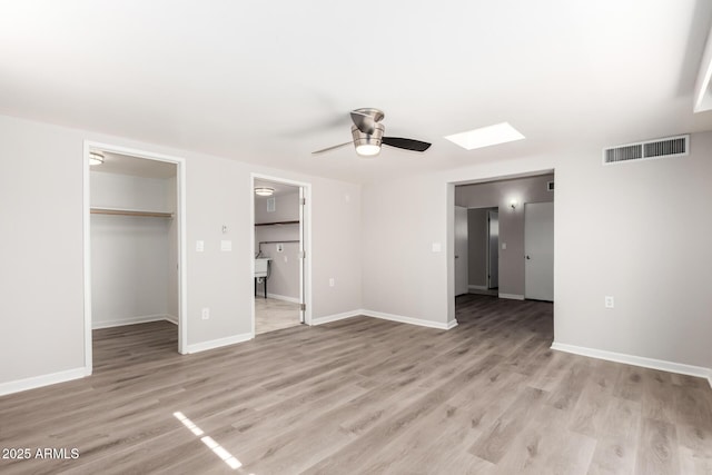 unfurnished bedroom with light wood finished floors, a skylight, baseboards, visible vents, and a walk in closet