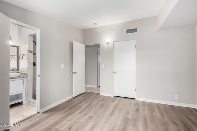 unfurnished bedroom with connected bathroom, a sink, visible vents, baseboards, and light wood-type flooring