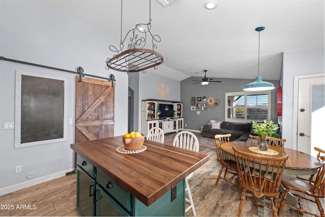 dining room with a barn door, lofted ceiling, ceiling fan, and light hardwood / wood-style flooring