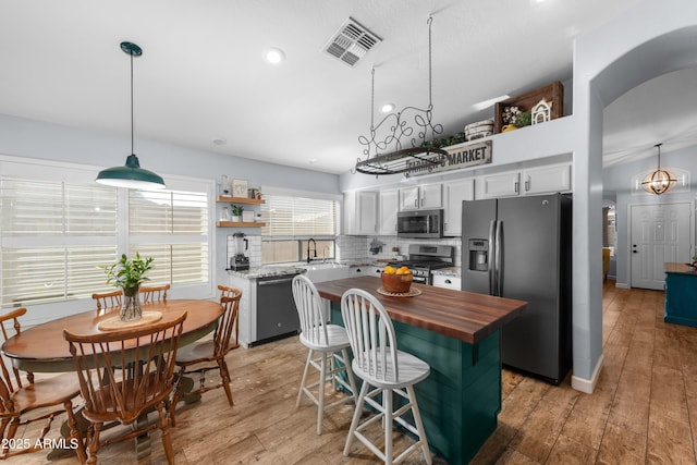 kitchen featuring butcher block countertops, decorative light fixtures, a center island, appliances with stainless steel finishes, and white cabinets