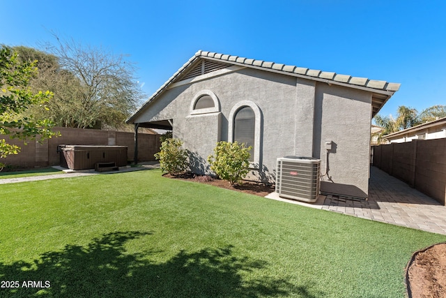 back of property with a hot tub, a patio, central AC unit, and a lawn