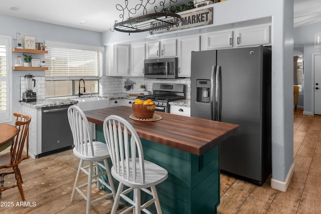 kitchen with stainless steel appliances, butcher block countertops, a kitchen island, and white cabinets