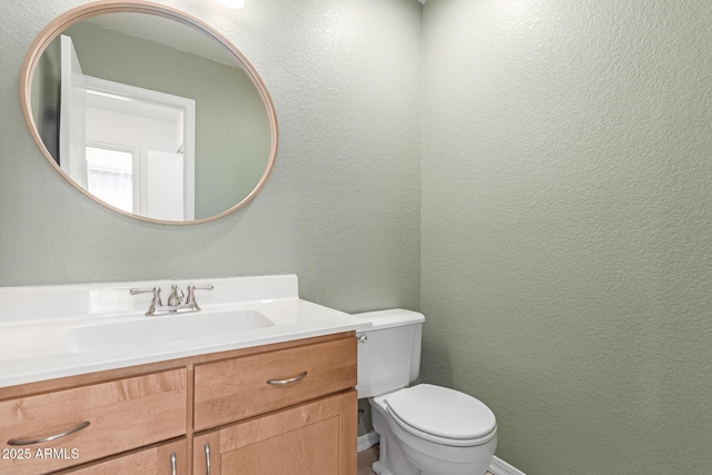 half bath with toilet, vanity, and a textured wall