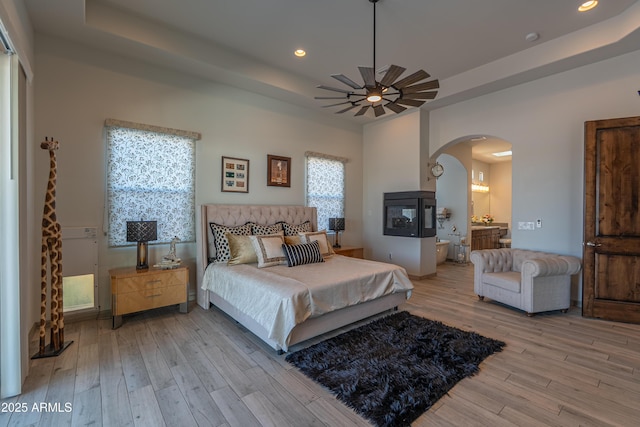 14332 E Bobwhite Way, Scottsdale, AZ 85262 - bedroom featuring a raised ceiling, arched walkways, light wood-style flooring, recessed lighting, and connected bathroom