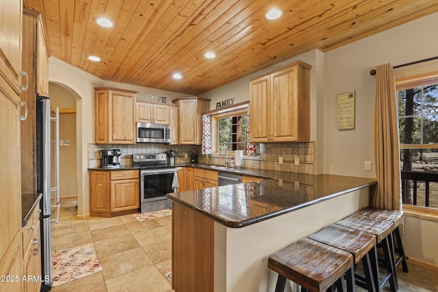 kitchen with appliances with stainless steel finishes, dark stone countertops, a kitchen breakfast bar, decorative backsplash, and kitchen peninsula