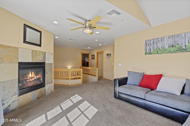 living room featuring a tiled fireplace, ceiling fan, and carpet