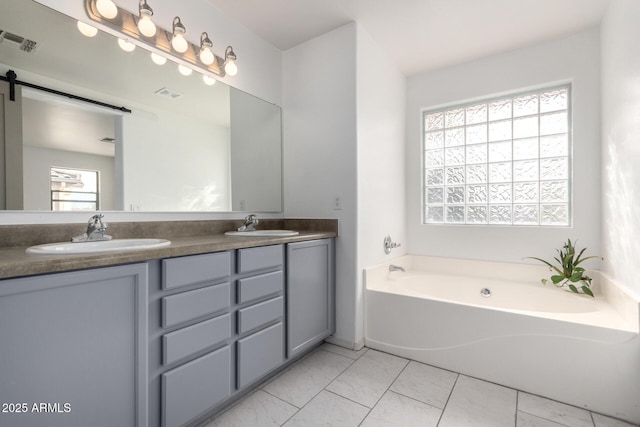 bathroom with a bath, double vanity, a sink, and visible vents