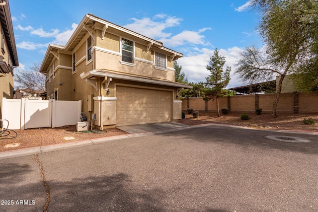 traditional-style house featuring driveway, an attached garage, fence, and stucco siding