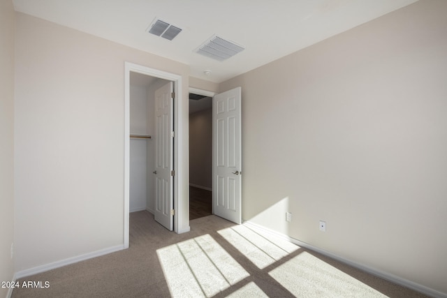 unfurnished bedroom featuring light colored carpet, a walk in closet, and a closet