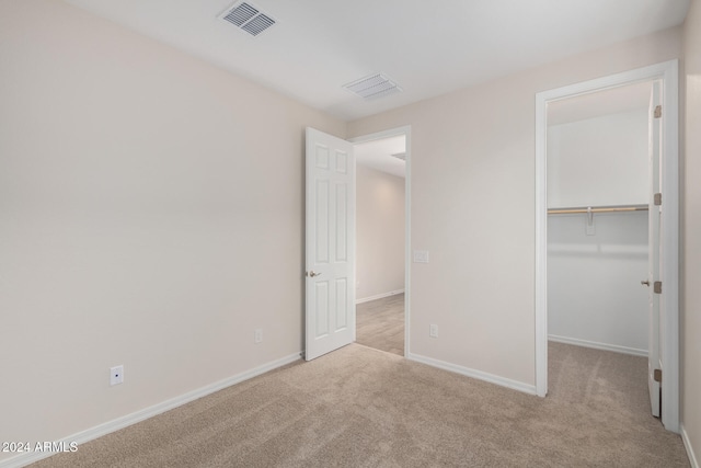 unfurnished bedroom with light carpet, a walk in closet, and a closet