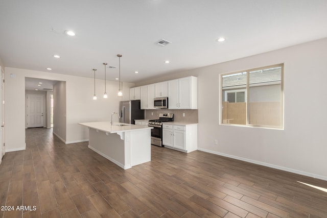 kitchen with white cabinetry, dark wood-type flooring, stainless steel appliances, decorative light fixtures, and a kitchen island with sink