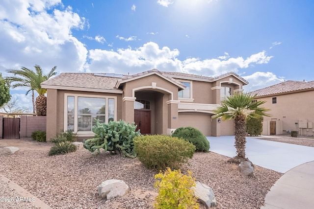 mediterranean / spanish home with stucco siding, an attached garage, roof mounted solar panels, fence, and driveway