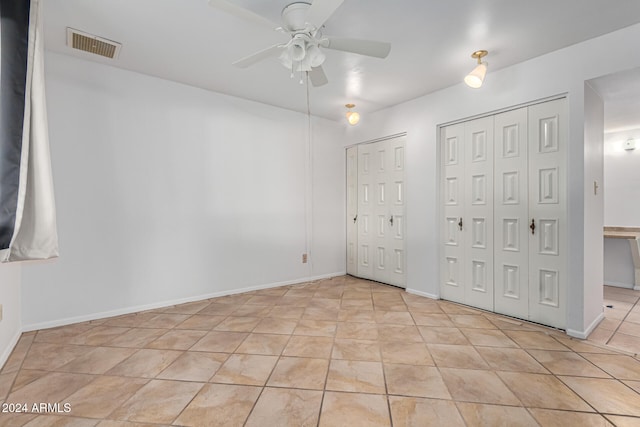 unfurnished bedroom with light tile patterned floors, two closets, and ceiling fan