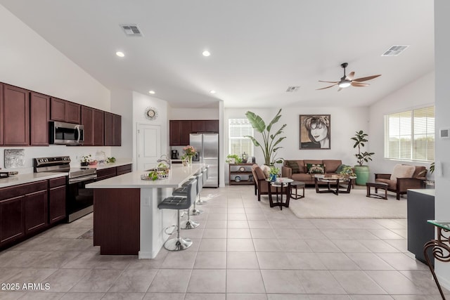 kitchen featuring a kitchen breakfast bar, stainless steel appliances, light tile patterned floors, a center island with sink, and lofted ceiling