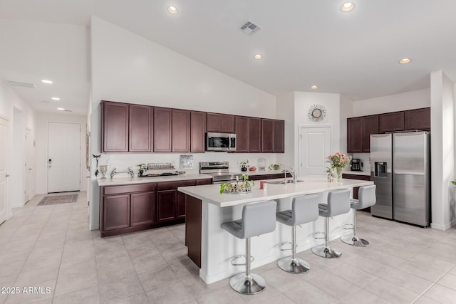 kitchen with high vaulted ceiling, a kitchen bar, a center island with sink, light tile patterned flooring, and appliances with stainless steel finishes