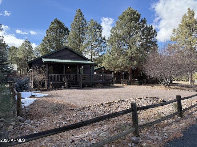 rustic home with metal roof, a porch, gravel driveway, and fence