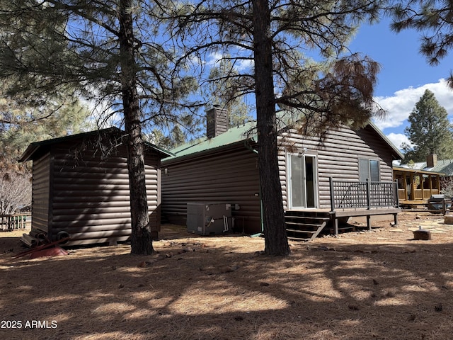 view of property exterior featuring a deck, log veneer siding, a chimney, and central air condition unit