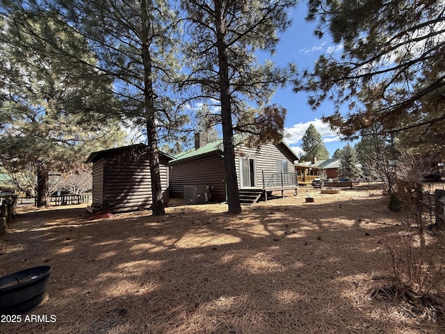 view of home's exterior featuring entry steps, a storage shed, faux log siding, a chimney, and an outbuilding