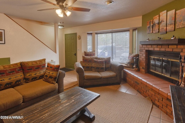 living room with ceiling fan, a fireplace, light tile patterned floors, and a textured ceiling