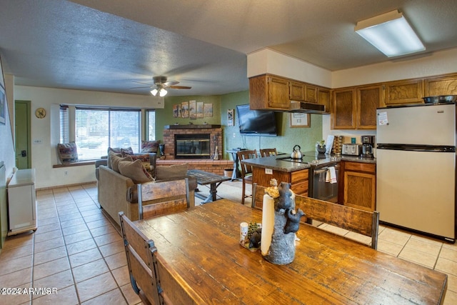 kitchen with ceiling fan, white fridge, a textured ceiling, a fireplace, and light tile patterned floors