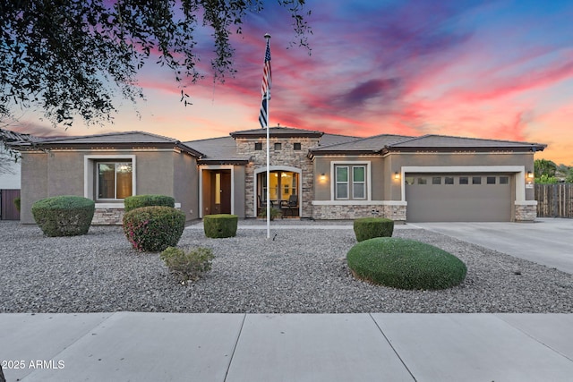 prairie-style home with stone siding, a garage, driveway, and stucco siding