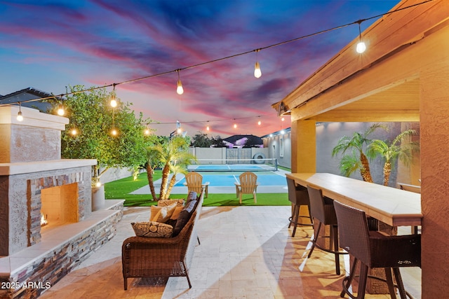 view of patio featuring a tennis court, a lit fireplace, and fence