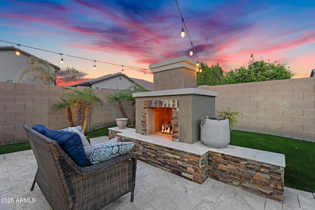 patio terrace at dusk with a warm lit fireplace and a fenced backyard