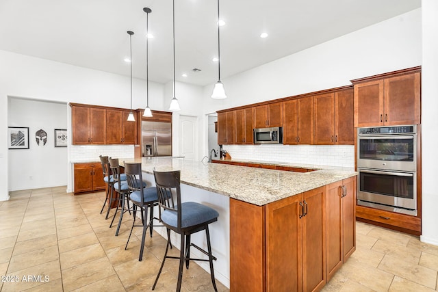 kitchen featuring a high ceiling, a large island with sink, decorative backsplash, appliances with stainless steel finishes, and decorative light fixtures