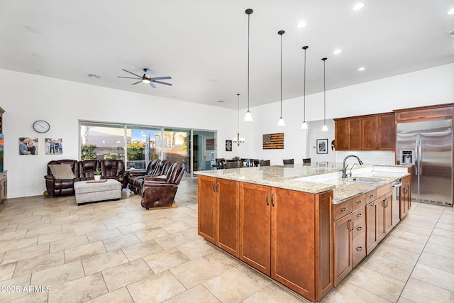 kitchen with a sink, backsplash, open floor plan, built in fridge, and a large island with sink