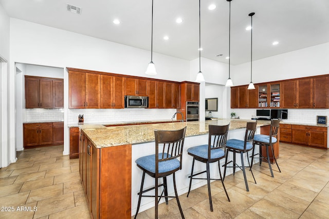 kitchen with visible vents, a sink, a spacious island, appliances with stainless steel finishes, and a towering ceiling