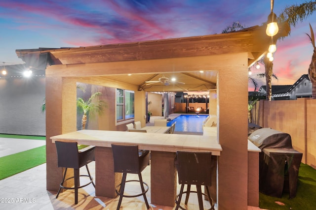 patio terrace at dusk with ceiling fan, a fenced backyard, a fenced in pool, and outdoor dry bar