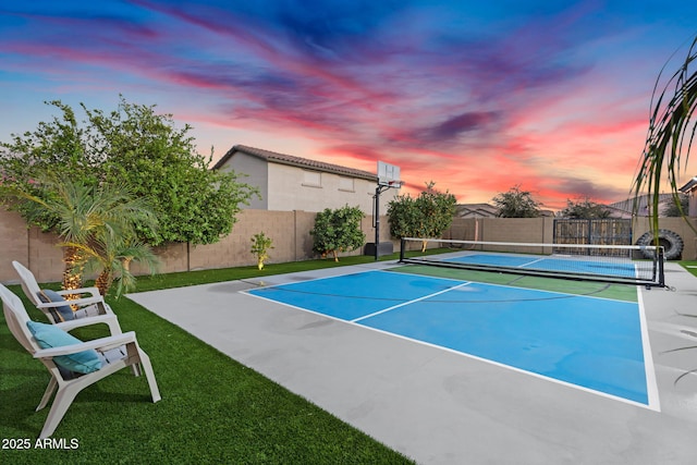 view of tennis court with a lawn and fence