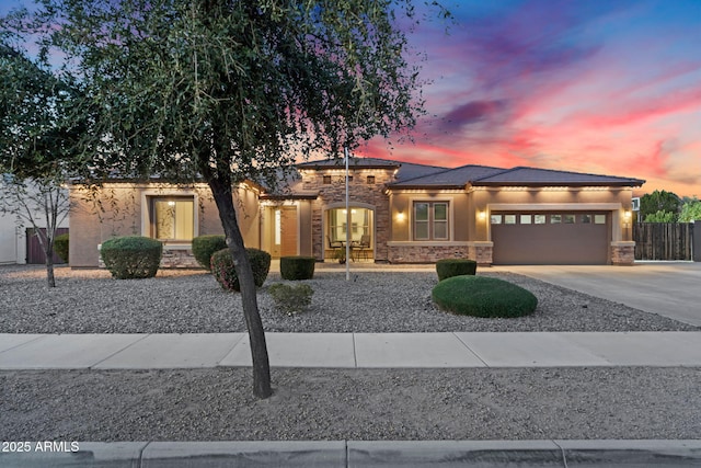 view of front of house featuring fence, concrete driveway, stucco siding, a garage, and stone siding