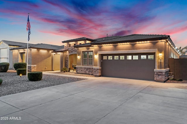 prairie-style home with stucco siding, driveway, stone siding, fence, and a garage